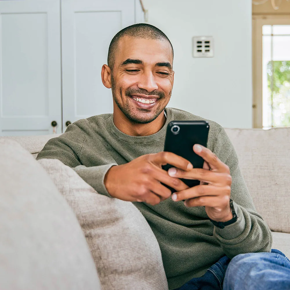 Man sitting on couch with cellphone smiling