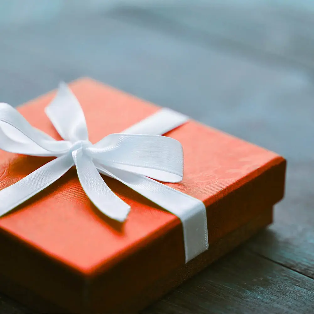 An orange gift box with white ribbon sits on a table.