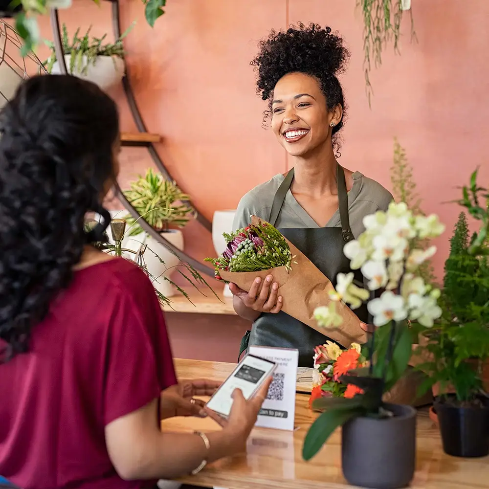 A flower shop attendant helps a woman checkout with contactless payment.